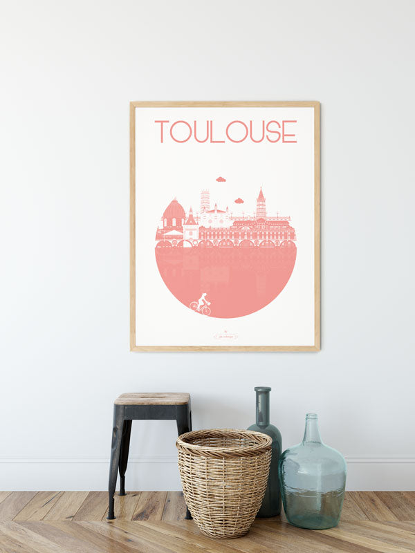 Affiche "Toulouse – La Ville" en rose accrochée au mur, accompagnée d'une plante verte et d'une table basse.